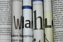 Mehrere eng nebeneinander aufgerollte Zeitungsseiten mit großen Buchstaben und angeschnittenen deutschen Texten.