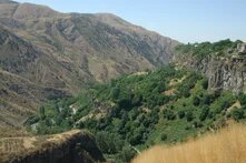 Green forest covers the slopes of a canyon, with rocky cliffs rising above the valley.