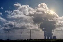 Windkraftanlagen und ein Kraftwerk unter dramatischen Cumuluswolken in einer ländlichen Landschaft.