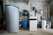 Mehrere Heizungs- und Speichergeräte mit vielen isolierten Rohren an einer Wand in einem Technikraum installiert.