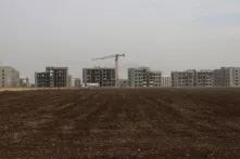 Eine Baustelle mit mehreren im Bau befindlichen Wohngebäuden. Im Vordergrund ein braches Feld, im Hintergrund ein Baukran.