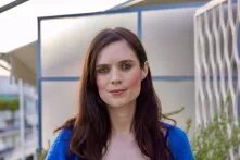 Porträt von Katy Fallon. Sie trägt ein blaues Oberteil und hat lange, dunkelbraune Haare.