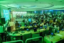  Ein Konferenzraum voller Teilnehmer*innen. Auf der Leinwand steht „Courage to Stand Up for Democracy“. Laptops und Mikrofone sind auf den Tischen.