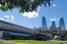 Modernes Gebäude mit Mustern im Vordergrund, dahinter die drei markanten Hochhäuser der Flame Towers in Baku.