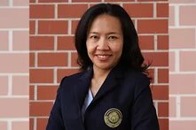 Photo: A person with long hair in a dark blazer, standing in front of a brick wall.