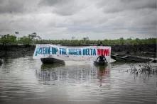 Aktivisten/innen auf dem Fluss mit Transparent "Clean-up the Niger Delta now"