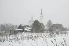 Russian village houses, barns and a church through a snow shower