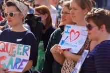 People on a rally for transgender equality, sign saying "queer for care"