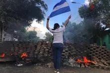 Eine Frau steht nahe einer brennenden Barrikade und hält die Staatsflagge von Nicaragua.
