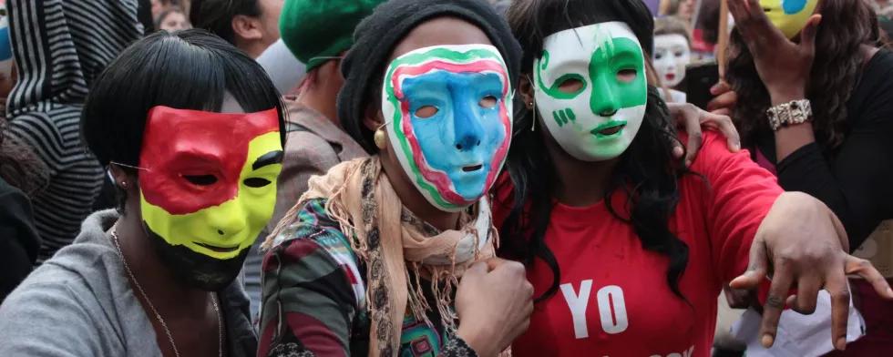 Menschen mit bunten Masken auf einer Demonstration, auf einem roten T-Shirt steht "Yo también soy puta" 
