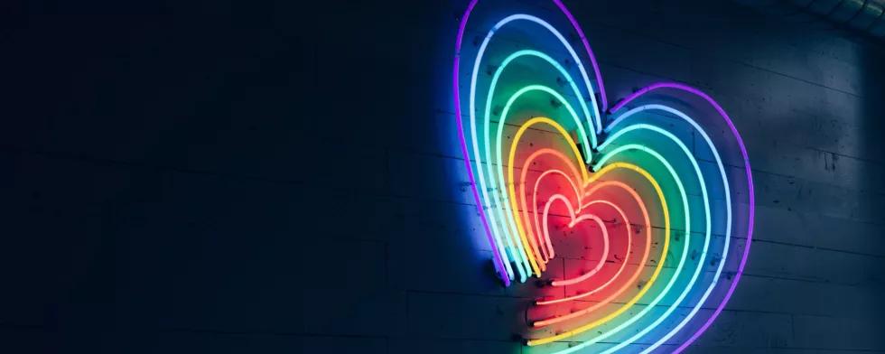 Ein leuchtendes Herz aus LEDs in Regenbogenfarben an einer dunklen Wand