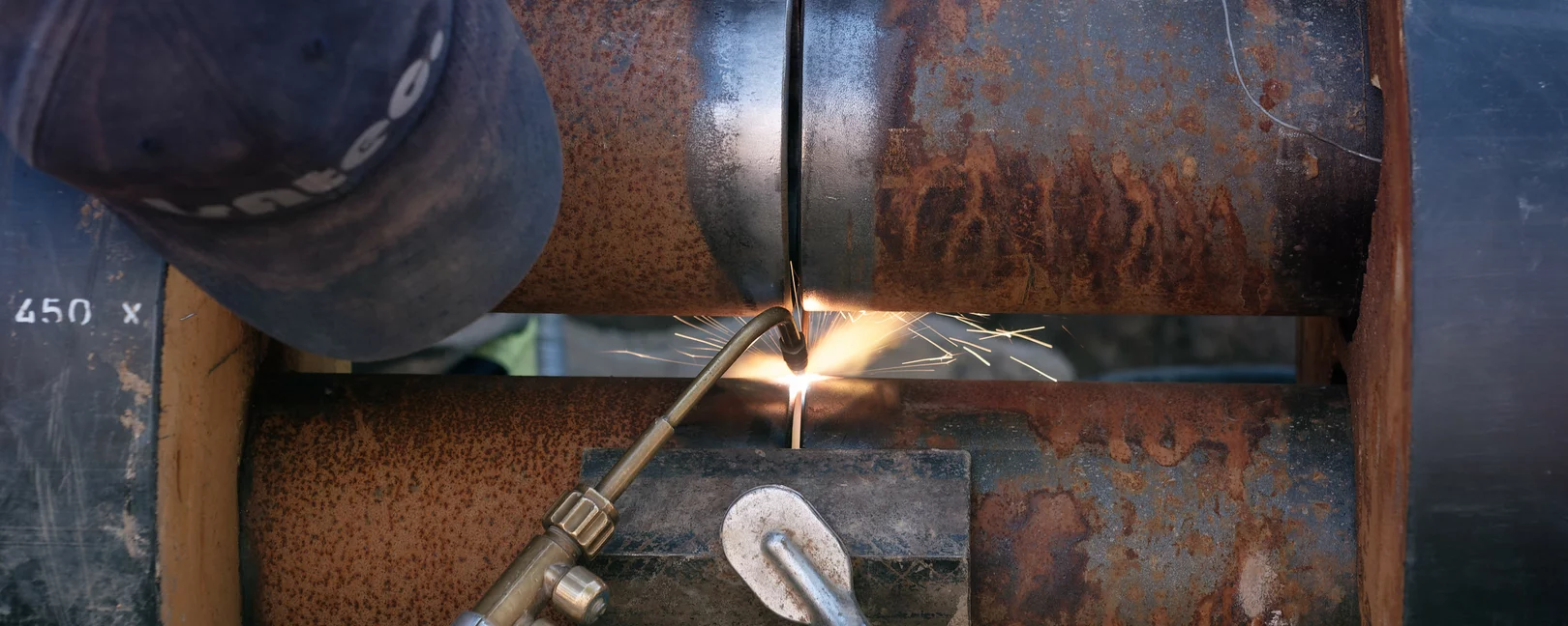 Ein Mensch schweißt mit einem Schweißgerät zwei Rohre zusammen