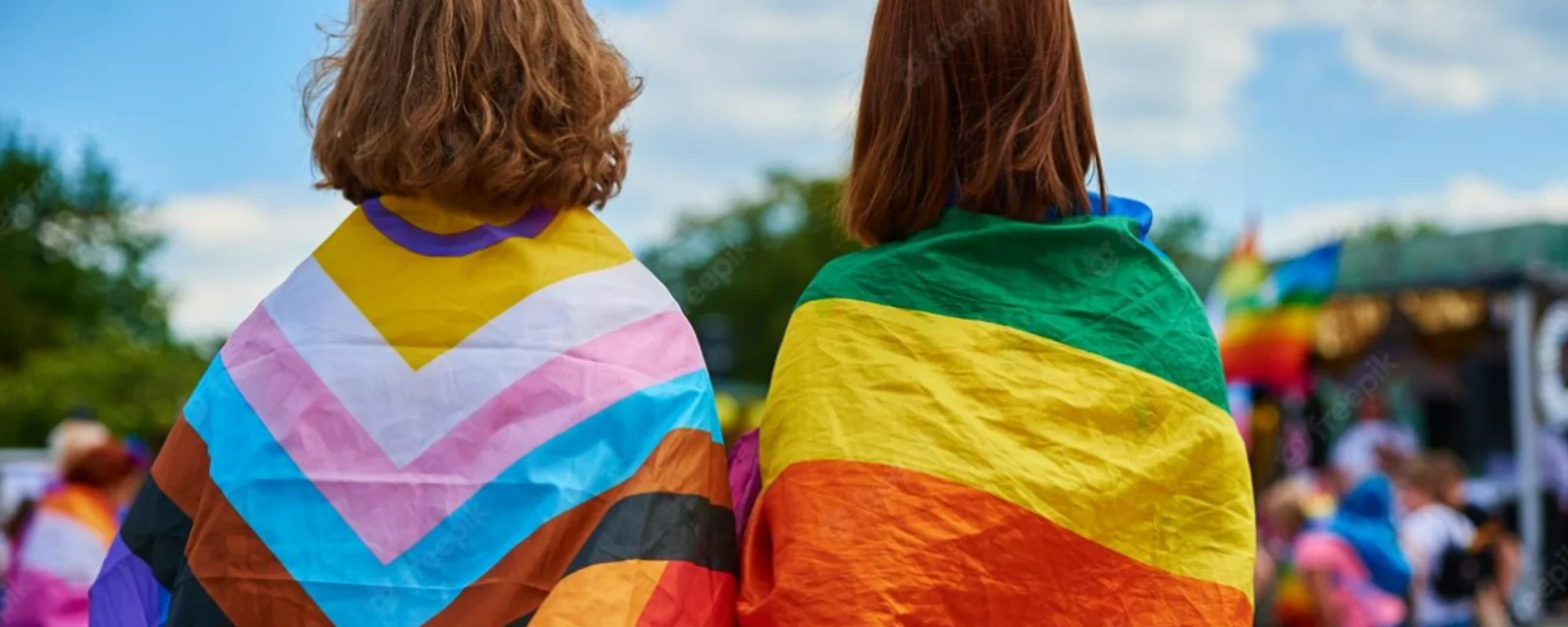 Zwei Menschen von hinten mit Queerfahnen als Umhang.