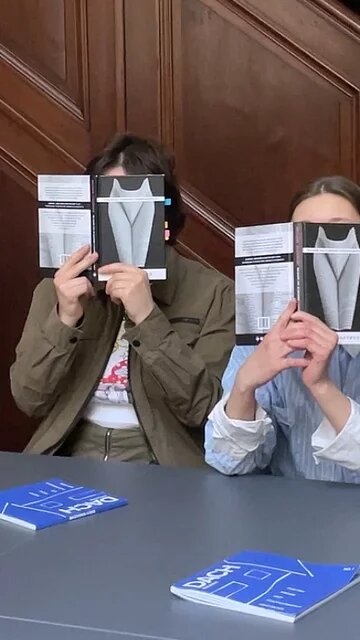 Das Foto zeigt vier Personen, die an einem Tisch sitzen und Flyer einer Veranstaltung vor ihr Gesicht halten.