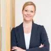 Kristina Weissenbach blickt lächelnd in die Kamera vor einem hellen, neutralen Hintergrund