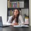 Porträt Diana González Pino. Sie sitzt vor einem Bücherregal