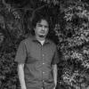 Portrait of Oswaldo Hernández. Black and white image. He is standing among trees.