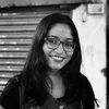 Photo: A smiling person with glasses and long hair stands in front of a closed shutter.