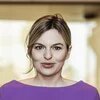Katharina Schulze Person steht frontal in Innenraum, schaut direkt in die Kamera, Hintergrund unscharf, Licht von hinten.