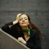 Shelly Kupferberg Person mit lockigem Haar lehnt am Betongeländer, stützt den Kopf mit der Hand und blickt ruhig in die Kamera.