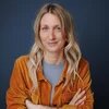 Svenja Borgschulte mit langen Haaren blickt in die Kamera, Arme verschränkt vor dunklem Hintergrund.