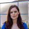 Porträt von Katy Fallon. Sie trägt ein blaues Oberteil und hat lange, dunkelbraune Haare.
