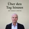Ein Mann mit grauem Haar steht vor einer Wand mit dem Text "Über den Tag hinaus mit Harald Grethe".