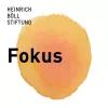 Der Text „Fokus“ steht groß vor einem unscharfen, orangefarbenen Kreis. Oben links steht „Heinrich Böll Stiftung“ auf weißem Hintergrund.