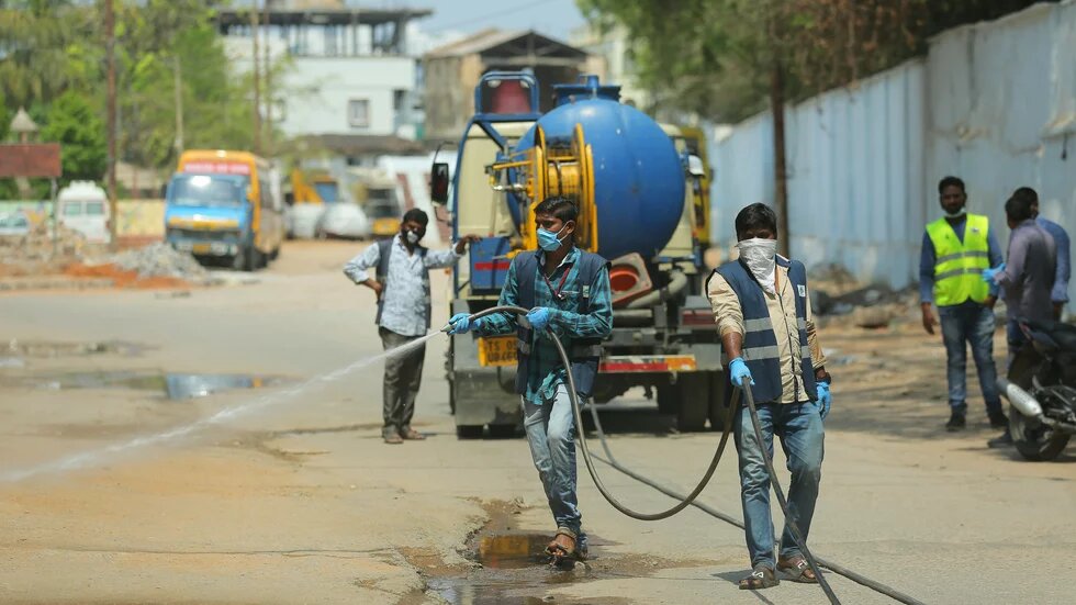 Männer mit Masken reinigen die leeren Straßen in einer Stadt in Indien mit Wasser