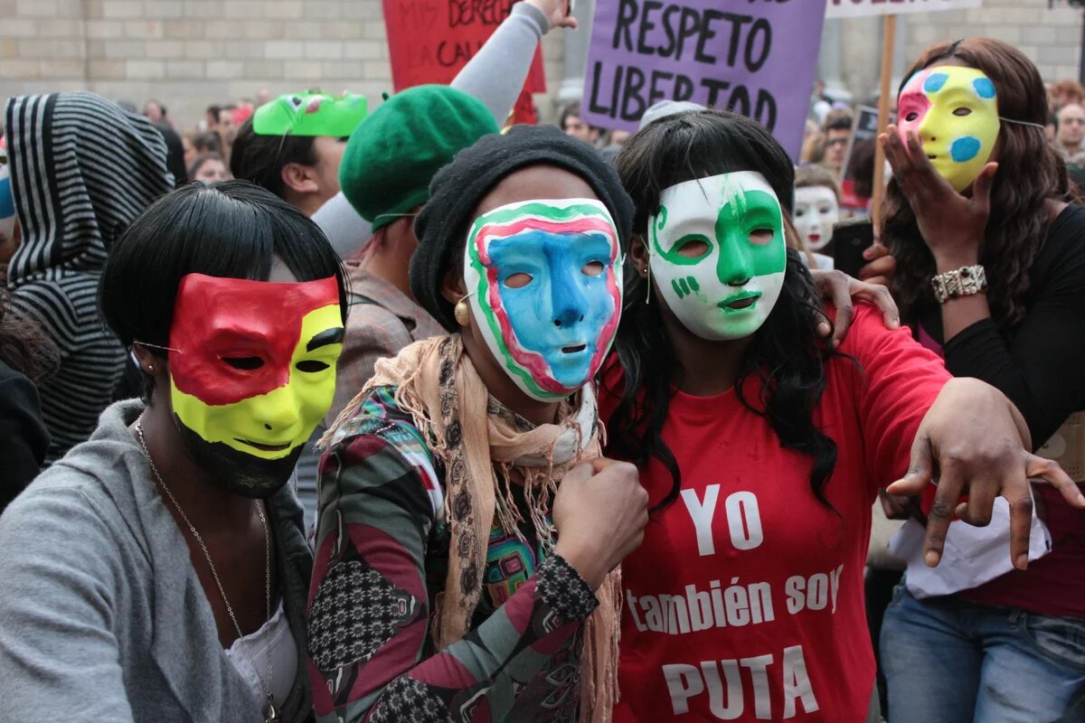Menschen mit bunten Masken auf einer Demonstration, auf einem roten T-Shirt steht "Yo también soy puta"