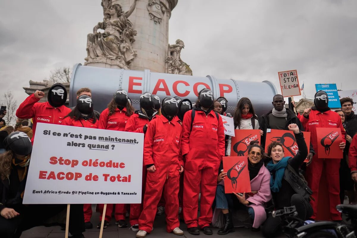 Eine Delegation ugandischer Aktivisten schließt sich dem STOP EACOP-Block beim Look UP-Klimamarsch in Paris, Frankreich, an, um das klimaschädliche Projekt von Total, die East Africa Crude Oil Pipeline, anzuprangern. Aktivisten in roten Squid-Game-Kostümen mit Total-Energies-Logo auf Masken halten eine gefälschte Pipeline, um Total aufzufordern, sich von fossilen Brennstoffen zu trennen.