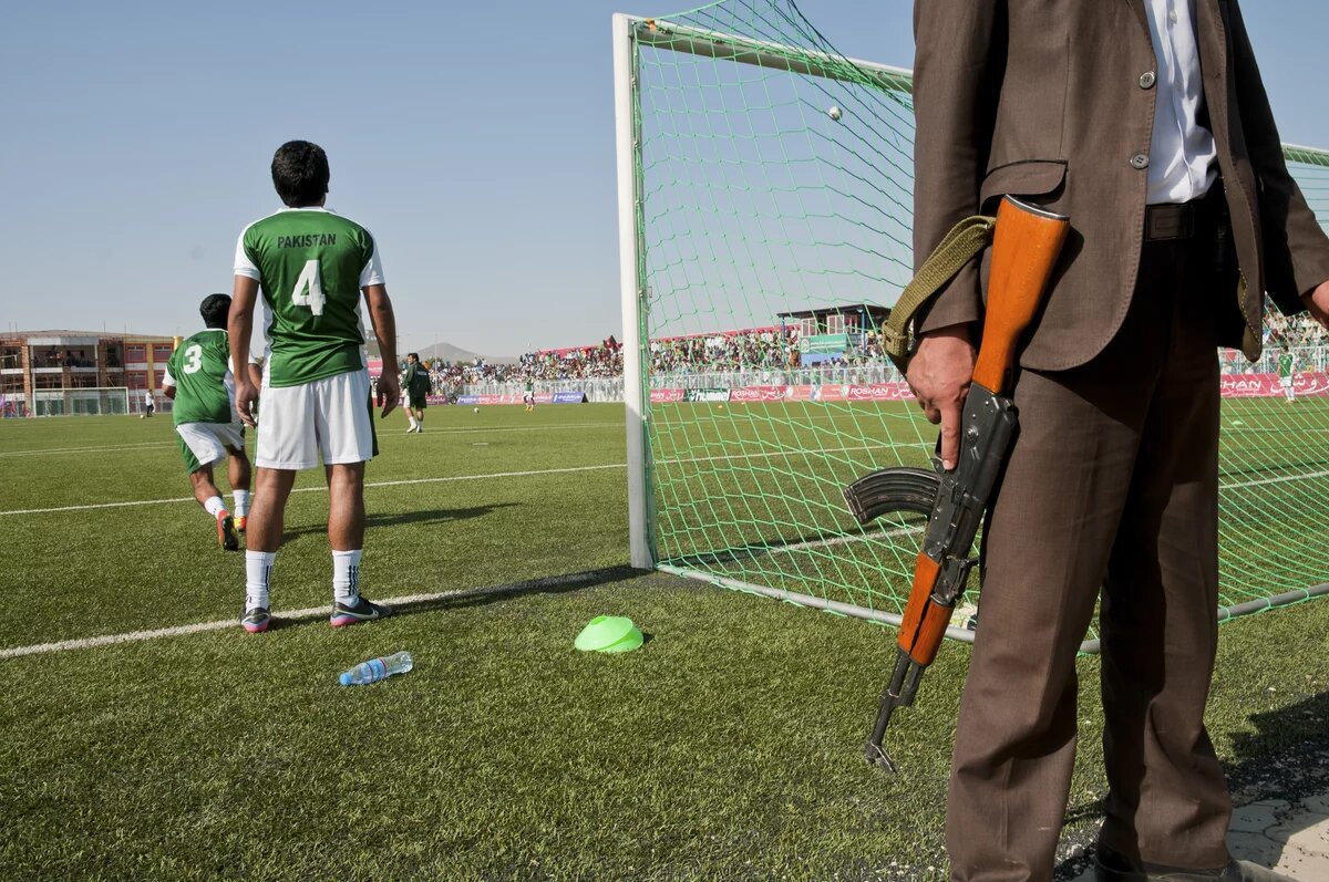 Ein Mann steht mit einem Gewehr hinter einem Tor auf einem Fußballplatz.
