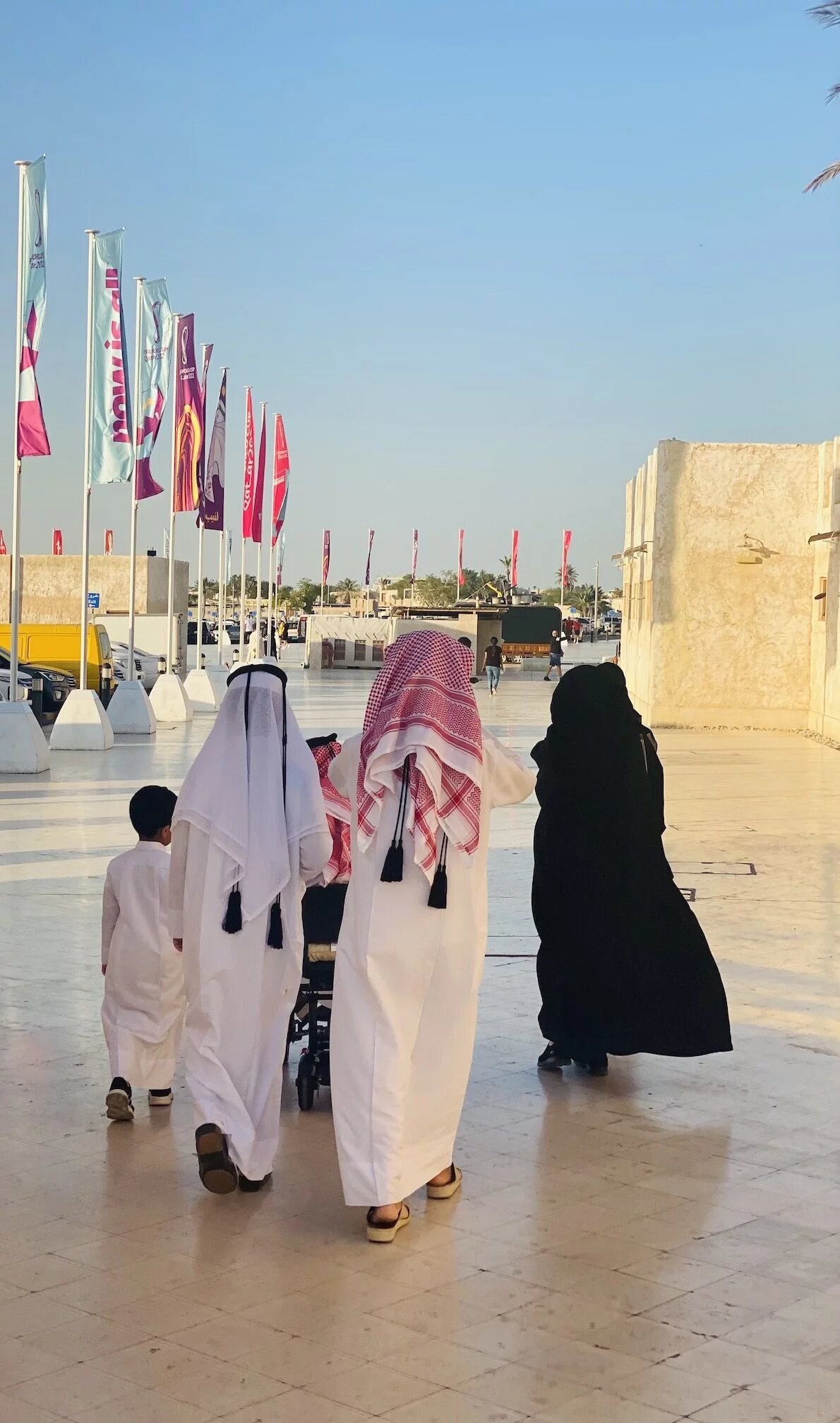 Es laufen Menschen in traditioneller Kleidung auf einem Gehweg in Katar