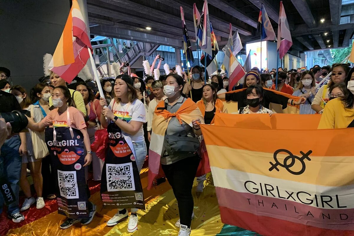 Pride 2022 in Bangkok Weiblich gelsene Personen mit Fahnen und Transparenten laufen über eien große Regenbogen-Fahne