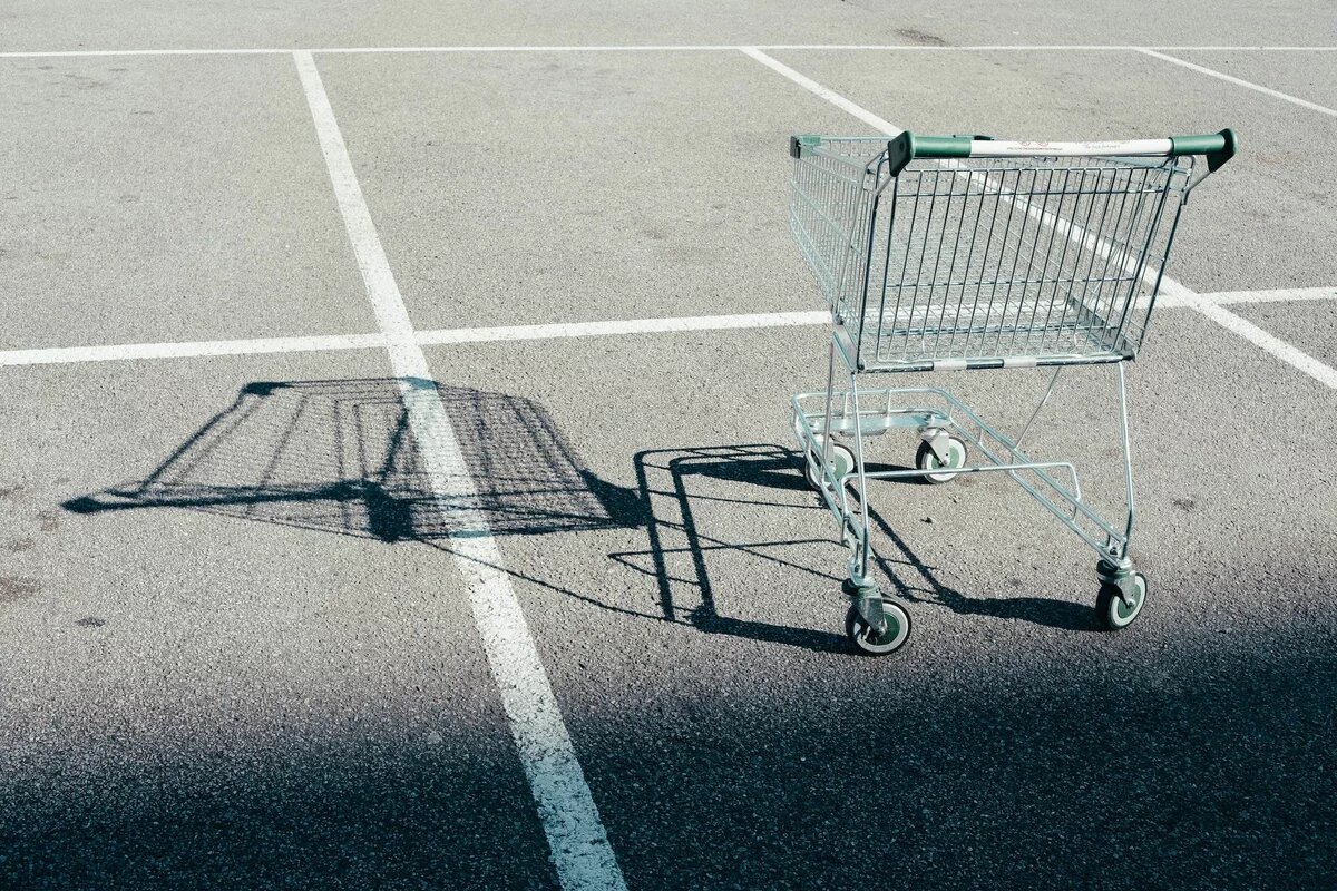 Ein leere Einkaufswagen steht auf einem leeren Parklatz und wirft einen langen Schatten