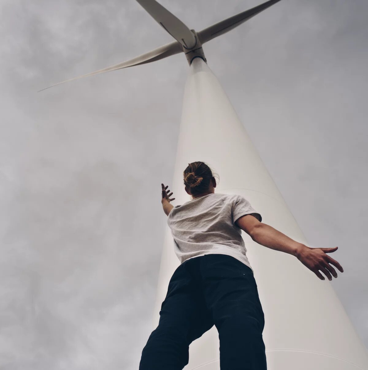 Eine Person steht unterhalb eines Windrads und reckt einen Arm in die Höhe