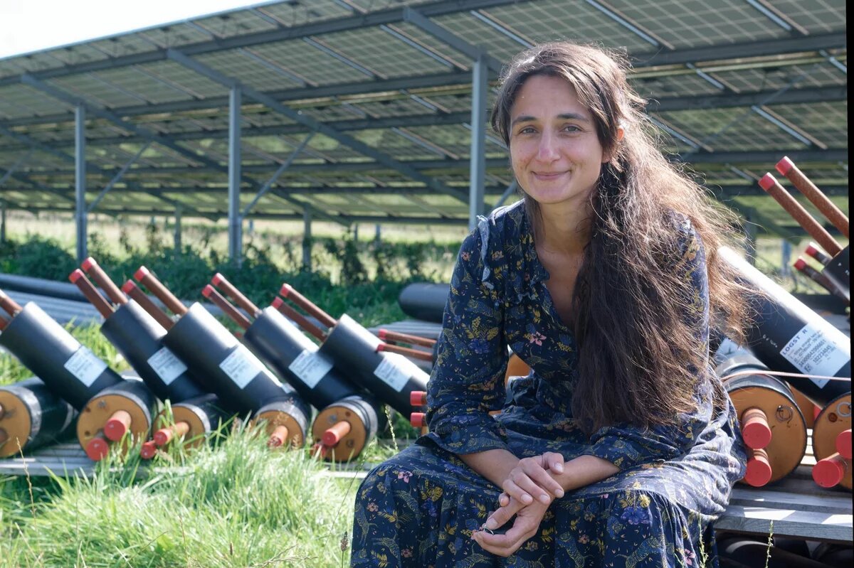 Emöke Kovač sitzt vor einem großen Solarpanel. Neben ihr zahlreiche Rohre, die verlegt werden sollen