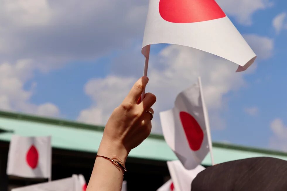 Kleine Japanische Flagge wird von einer Hand hochgehalten.