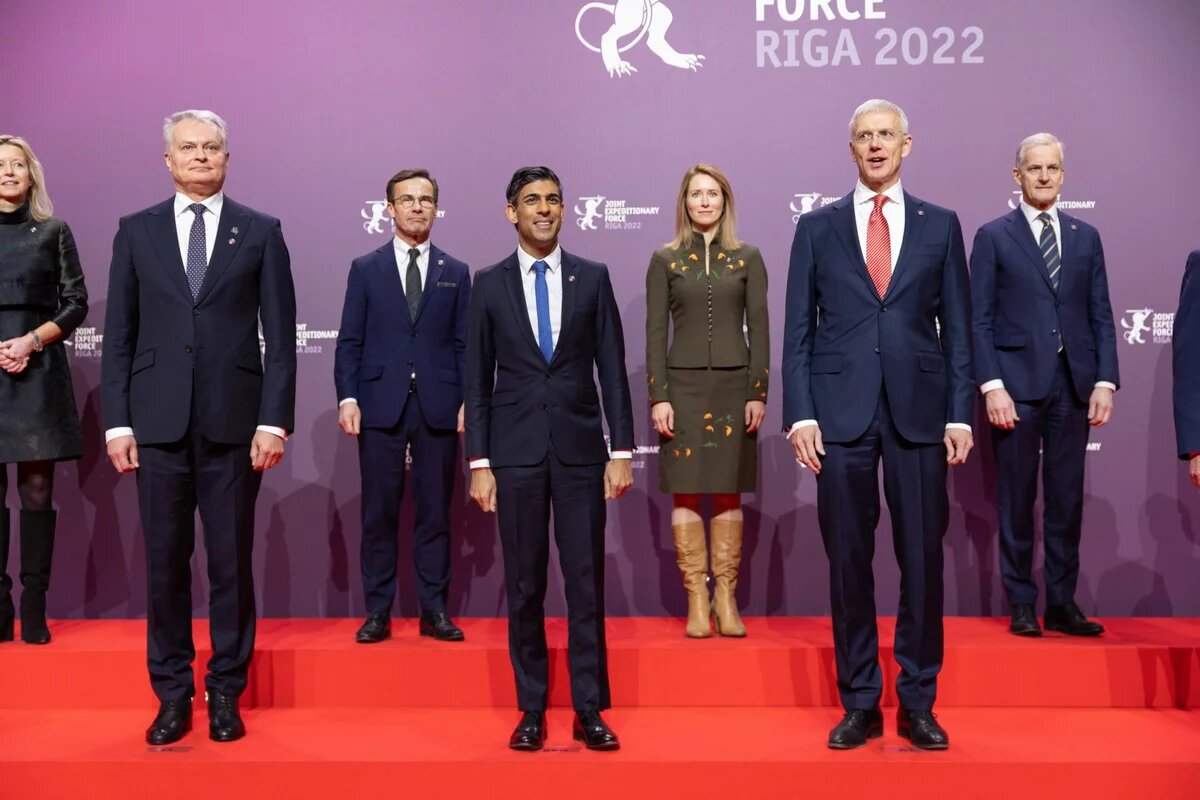 Joint Expeditionary Force Summit in Riga, Latvia. Excerpt from a group photo: Two women and six men stand together on a red staircase in front of a purple wall
