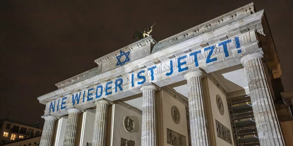 Brandenburger Tor angestrahlt mit Schriftzug "Nie wieder ist jetzt" und Judenstern