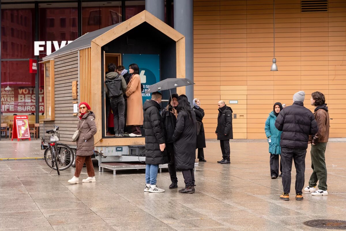 Mehrere Menschen, manche mit einem Regenschirm, stehen vor dem Tiny House am Potsdamer Platz.