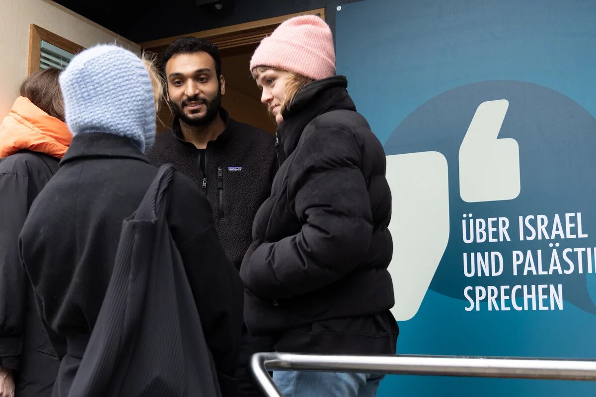Ahmad Dakhnous steht im Eingang des Safe Place. Auf einem blauen Schild steht "Über Israel und Palästina sprechen"