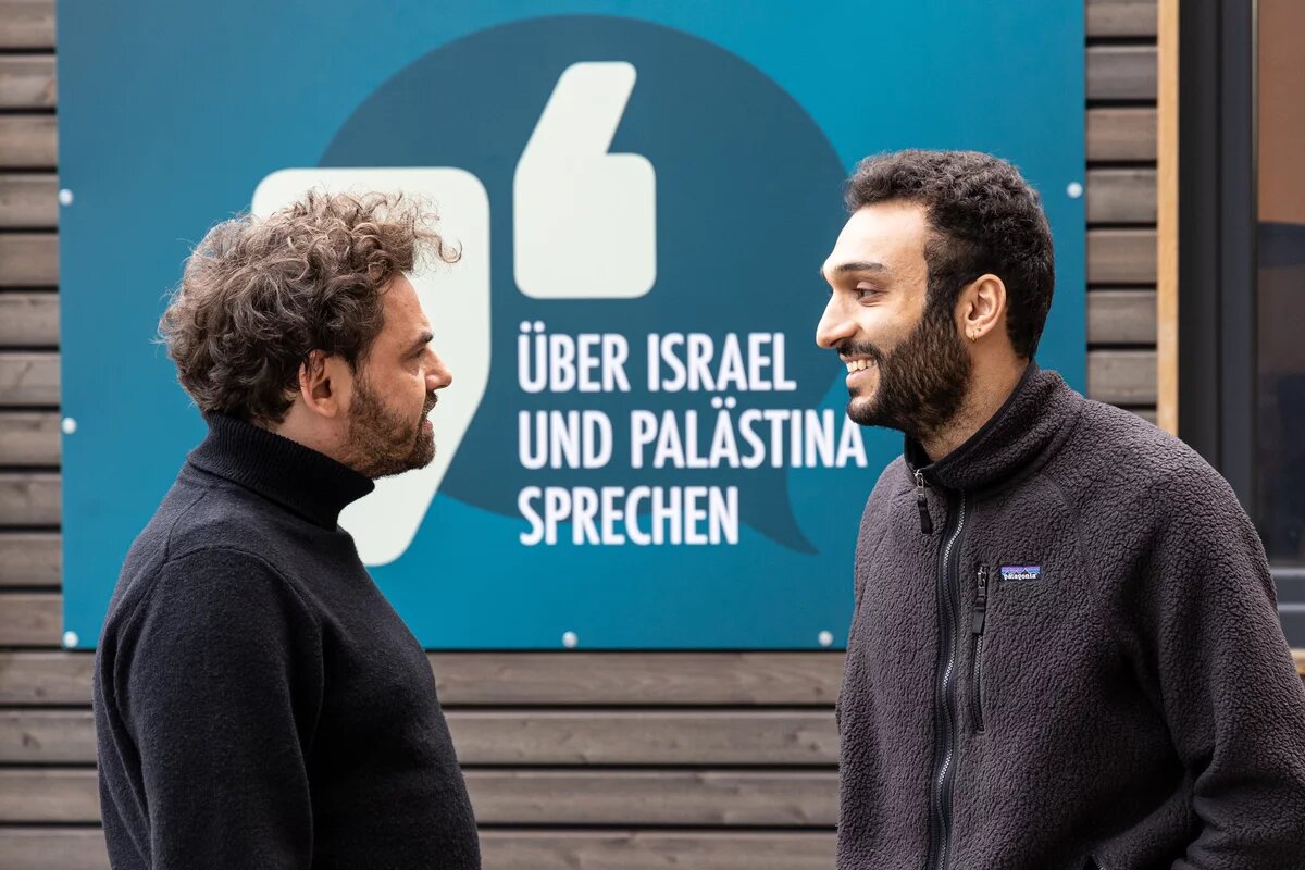 "Über Israel und Palästina sprechen" - Shai Hoffmann und Ahmad Dakhnous Shai Hoffmann und Ahmad Dakhnous stehen vor Eingan des Safe Place. Auf einem blauen Schild steht "Über Israel und Palästina sprechen"