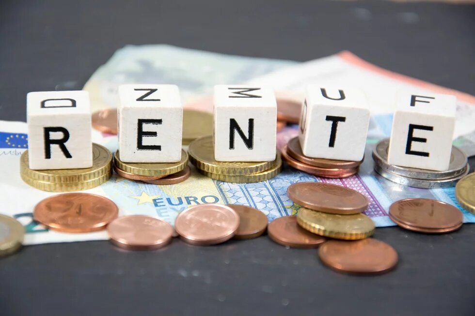 Rente Fünf mit Buchstaben bedruckte weiße Würfel formen das Wort RENTE. Unter den Würfeln liegen Euro-Münzen und mehrere Geldscheine.