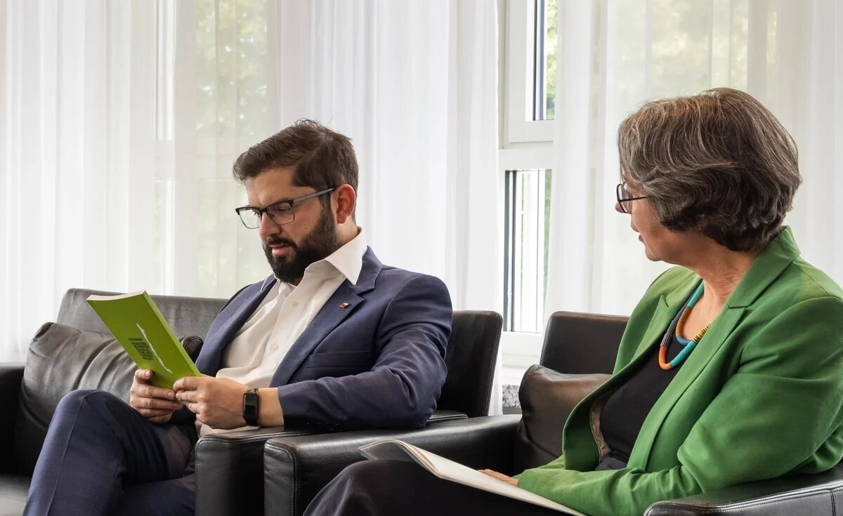 Gabriel Boric und Imme Scholz am 11. Juni 2024 in Berlin. Gabriel Boric, Präsident Chiles, sitzt auf einem dunklen Sofa und hält eine grüne Publikation in der Hand. Neben ihm sitzt Imme Scholz, Vorstand der Heinrich-Böll-Stiftung.