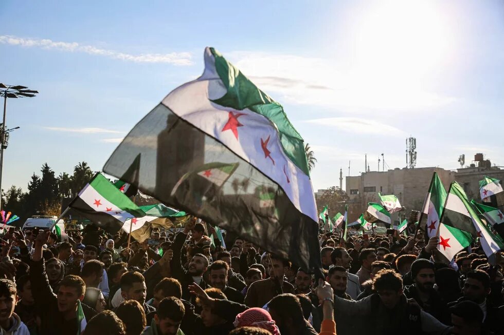 Aleppo, Syrien, 13. Dezember 2024. Foto: Menschenmenge bei einer Kundgebung, viele syrische Oppositionsflaggen werden hochgehalten, Sonnenschein im Hintergrund.