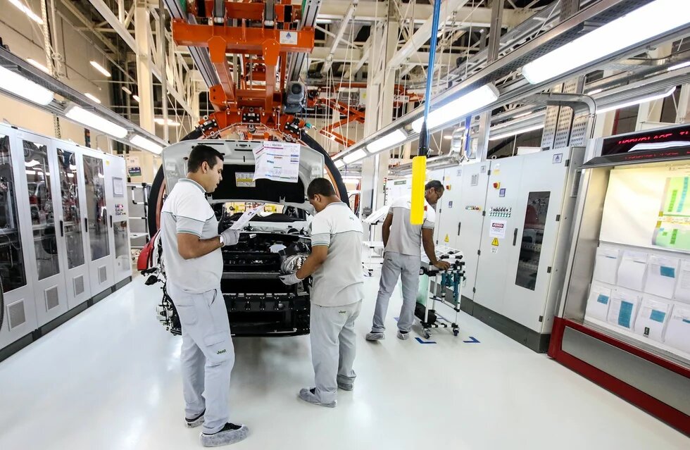 Jeep-Montage in Goiana, Brasilien Foto: Drei Personen arbeiten an einem Fahrzeug in einer Fabrikhalle. Im Hintergrund Maschinen und technische Geräte.