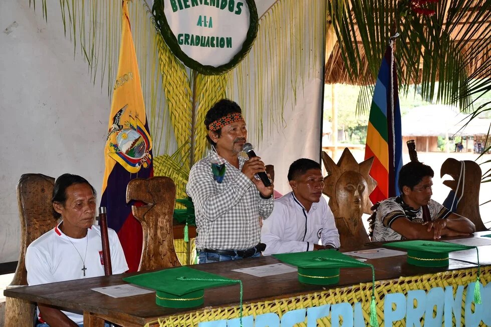 Sarakayu, die "Verteidiger:innen des Waldes", Ecuador. Menschen sitzen und stehen an einem langen Tisch, es sind die Sarakayu, die "Verteidiger:innen des Waldes", in Ecuador.