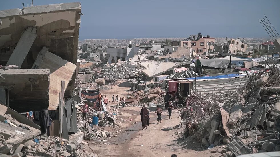 Gaza Photo: Destroyed buildings and rubble in Gaza, several people walking along a dusty road.