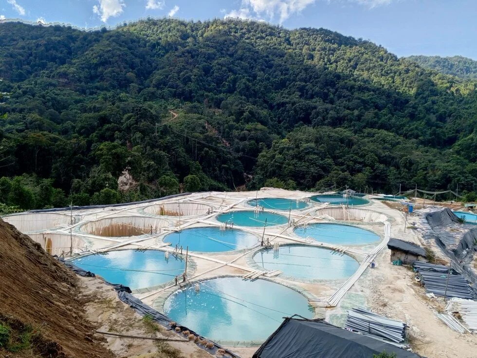 Rare earth mining in Hpyi Di Village near Mai Ja Yang town, Kachin State, Myanmar Photo: In a valley near a forested hill, several round water basins with light blue liquid and white pipelines are visible.